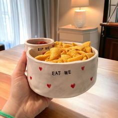 a person holding up a bowl filled with cheetos and ketchup on the side