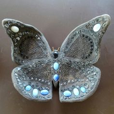 a butterfly shaped object sitting on top of a metal surface with blue and white beads