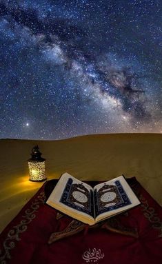 an open book sitting on top of a blanket in the desert under a night sky filled with stars