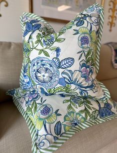 a blue and green floral pillow sitting on top of a couch next to a wall