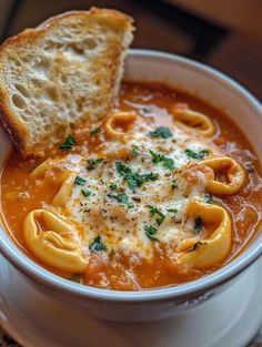 a white bowl filled with pasta soup and a piece of bread on top of it