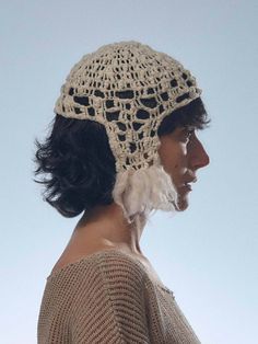 a woman wearing a crocheted hat with feathers on it's side and the top part of her head