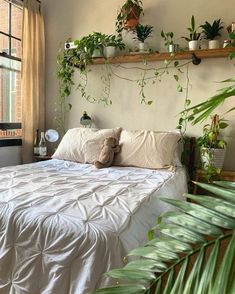 there is a bed with white sheets and plants on the headboard