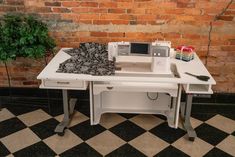 a sewing machine sitting on top of a table next to a potted plant in front of a brick wall