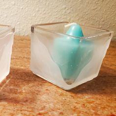 two glass containers sitting on top of a counter next to each other with a blue candle in them