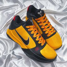 a pair of yellow and black nike shoes on a white satin sheeted bed spread