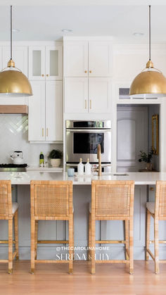 a kitchen with white cabinets and gold pendant lights