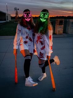 two people with neon masks on their faces and holding baseball bats in front of an orange sky