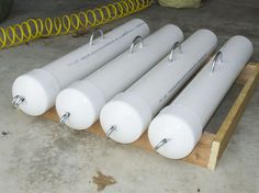 four white cylinders are lined up on a wooden pallet with yellow springs in the background