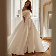 a woman in a white wedding dress standing by a mirror and looking at the camera