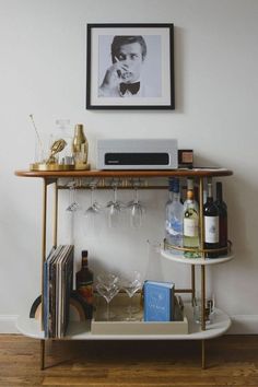 a bar cart with wine glasses and liquor bottles on it in front of a framed photograph