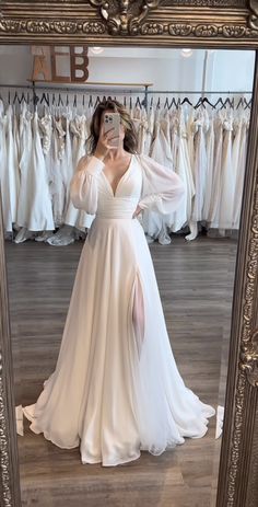 a woman taking a selfie in front of a mirror wearing a wedding dress with long sleeves