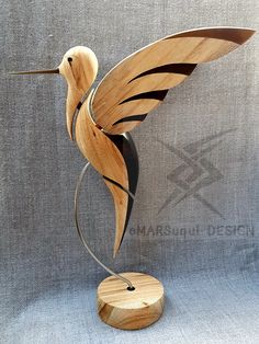 a wooden bird sculpture sitting on top of a metal stand next to a gray wall