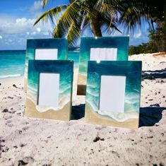 two frames sitting on top of a sandy beach next to the ocean and palm trees