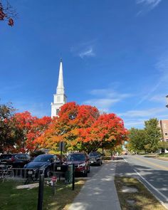 a church steeple in the background with cars parked on the side of the road