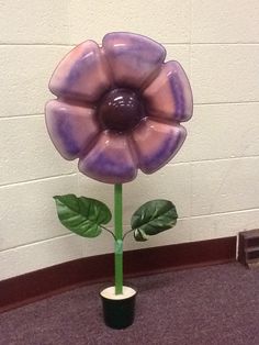 a purple flower sitting on top of a green plant in a room next to a white wall