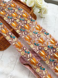 three pieces of purple and gold embroidered fabric with flowers on the side, next to a wicker basket