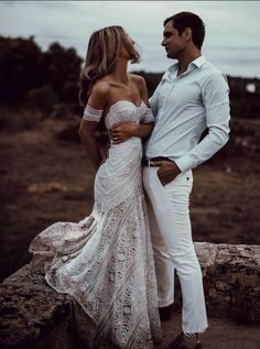 a man and woman standing next to each other on top of a rock in front of the ocean