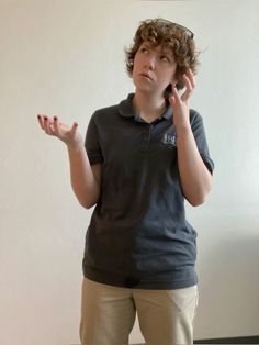 a young man standing in front of a white wall holding his hands up to his ear