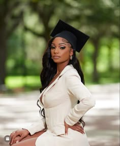 a woman in a graduation cap and gown sitting on the ground with her hands on her hips