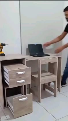 a man standing next to a desk with a laptop computer on it and drawers underneath