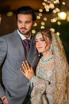 a man and woman dressed in wedding attire posing for a photo with lights behind them