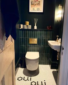 a bathroom with a toilet and sink in it's stall, next to a green tiled wall