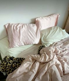 an unmade bed with pink sheets and leopard print blankets on it, next to a window