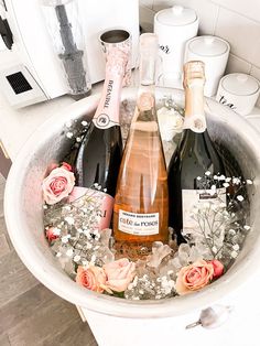 three bottles of champagne in a bucket with flowers on the side and two empty wine glasses