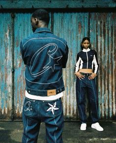 two people standing next to each other in front of a rusty wall