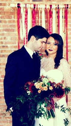 a bride and groom standing next to each other in front of a red brick wall