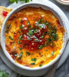 a white bowl filled with cheese and sauce on top of a plate next to bread