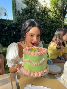 a woman blowing out candles on a cake with other people in the back ground behind her