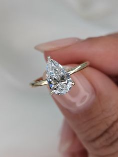 a woman's hand holding an engagement ring with a pear shaped diamond