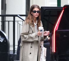 a woman is holding a coffee and walking down the street