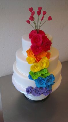 a multi - tiered wedding cake with rainbow flowers on the top and bottom layer