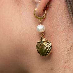 Get ready to shine with the Charleston Earrings! These gold-colored huggie earrings are pure coastal charm, featuring delicate pearl accents and adorable gold sea shell charms. Perfect for adding a touch of beachy elegance to any outfit, the Charleston Earrings will have you dreaming of sun-soaked shores and salty sea breezes. Whether you're out for a stroll by the beach or just wishing you were, these earrings bring a splash of ocean fun wherever you go. Slip them on and let the seaside magic b Gold Shell-shaped Pearl Earrings Ocean-inspired, Gold Pearl Drop Earrings With Ocean-inspired Style, Ocean-inspired Gold Pearl Earrings For Beach, Summer Gold Dangle Pearl Earrings, Gold Dangle Pearl Earrings For Summer, Gold Pearl Charm Earrings For Beach, Gold Pearl Earrings For Beach, Gold Pearl Earrings With Charm For Beach, Gold Shell Earrings With Pearl Charm