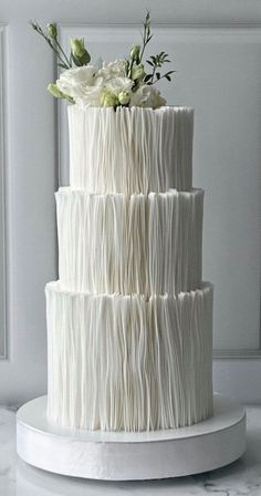 a three tiered cake with white icing and flowers on the top is sitting on a table