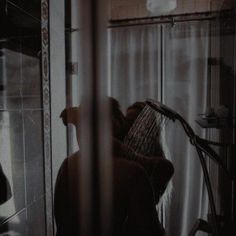 black and white photograph of a woman brushing her hair in front of a shower stall