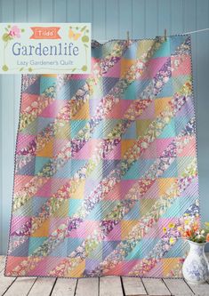 a quilt on a clothes line next to a potted plant and vase with flowers