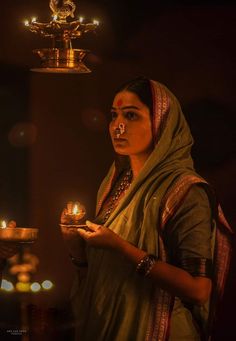 a woman holding a lit oil lamp in her hand and looking at the camera with an evil look on her face