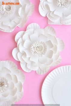 paper flowers are arranged on a pink background with white plates in the middle and bottom