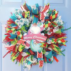 a colorful christmas wreath hanging on a blue door with red, white and green ribbons