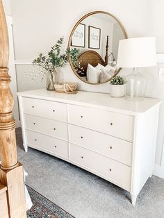 a white dresser topped with lots of drawers and a round mirror on top of it