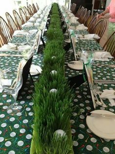 a long table is set with place settings and green grass in vases on the tables