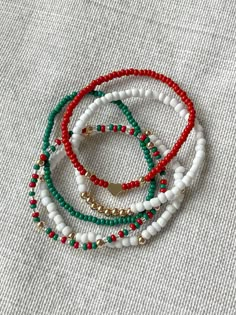 three bracelets with red, white and green beads on top of a gray surface