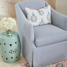 a blue chair sitting next to a vase with flowers in it and a rug on the floor