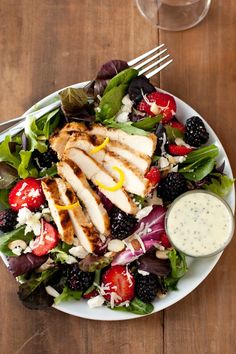 a salad with chicken, berries, and dressing on the side is ready to be eaten