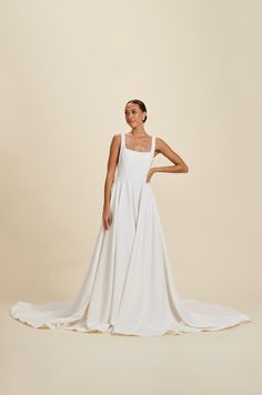 a woman in a white wedding dress standing on a beige background with her arms behind her back