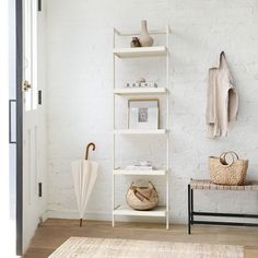 a white shelf with an umbrella and other items on it next to a chair in front of a brick wall